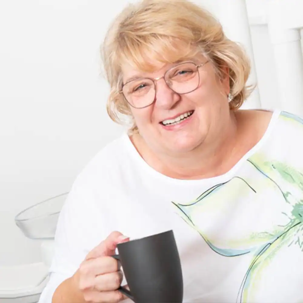Seniorin trinkt Kaffee, lächelnd, in gemütlicher Umgebung.