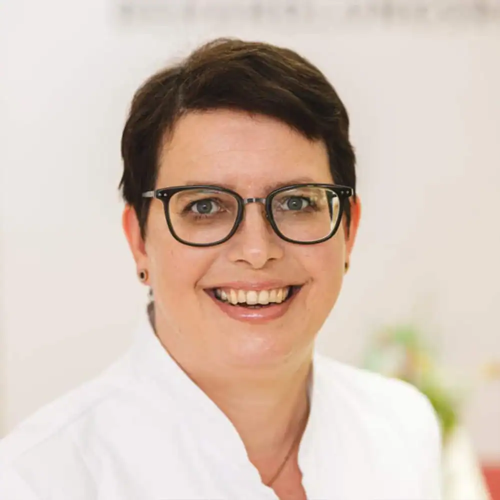 Frau mit Brille und freundlichem Lächeln, medizinisches Personal.