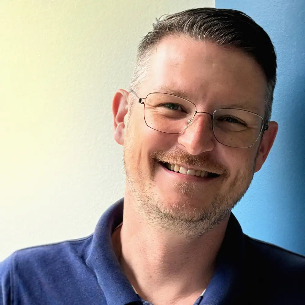 Mann mit Brille und freundlichem Lächeln, professionell und vertrauenswürdig.