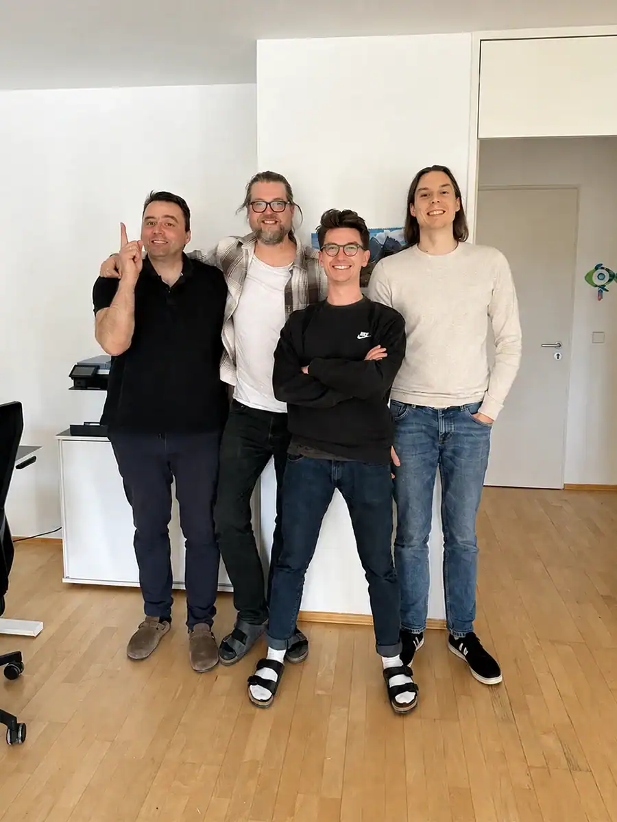 Vier Personen stehen im Büro, lächeln und posieren für das Foto.